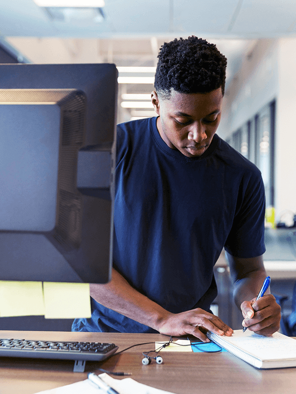 Homem fazendo anotações em um caderno com um computador na frente